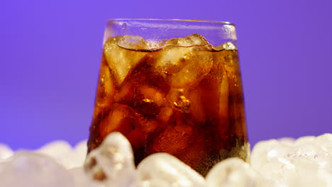 Close-Up-Of-Chilled-Cold-Drink-In-Glass-Being-Mixed-On-Ice-Cubes-Against-Purple-Background